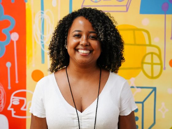 Thaís Marcelino diante de um painel colorido, sorrindo para a câmera.